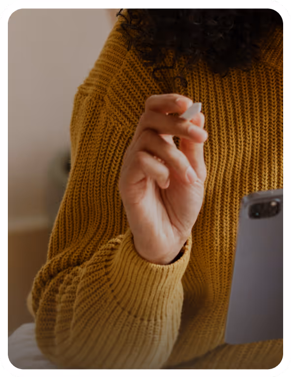 Woman in a yellow sweater holding a smartphone while taking notes.