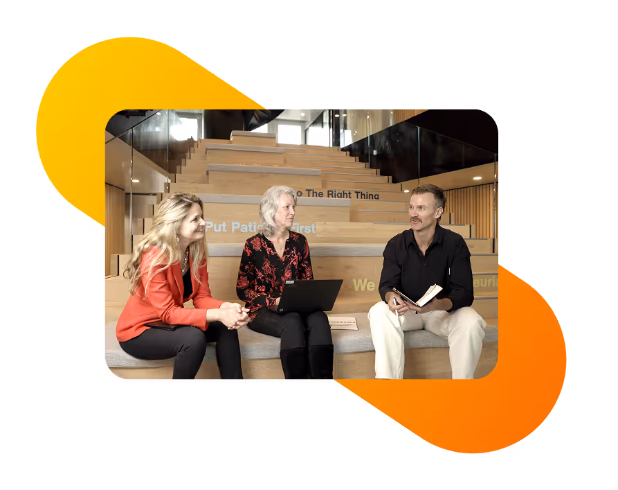 Three professionals sitting on wooden steps in a modern office, engaged in discussion with a laptop and notebook, representing Evinova’s collaborative consulting approach.